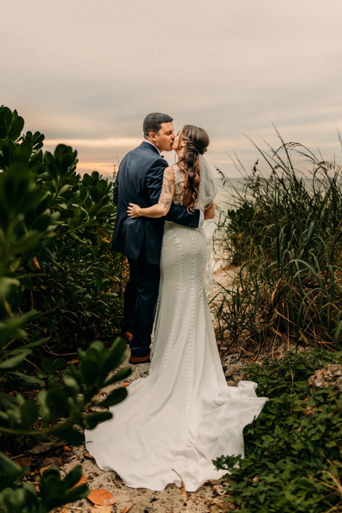Wedding Photographer, a bride and groom kiss on a trail leading to the ocean