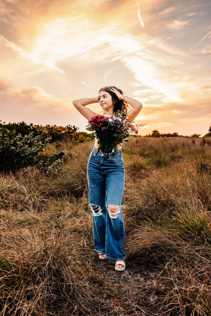 siesta key, senior photographer, a senior in a field at the beach with a bouquet of flowers at sunset
