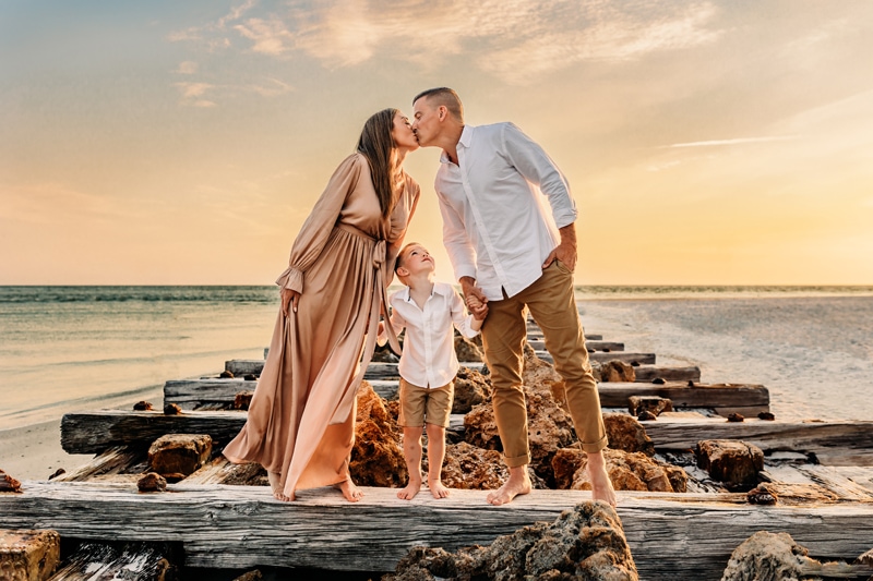 Anna Maria Island, family photographer, husband and wife kissing and their kid looking at them on the beach at sunset